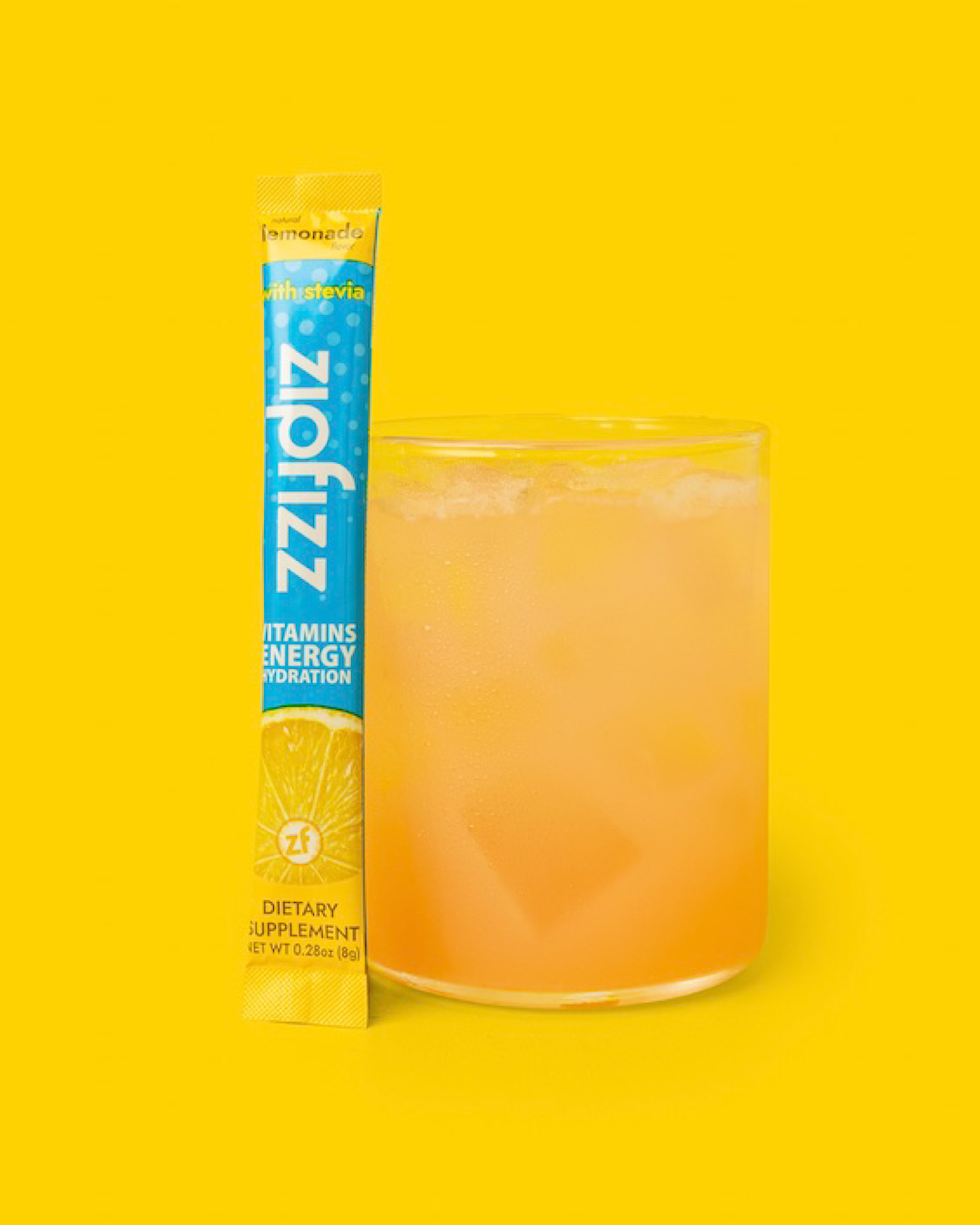 ZippFizz vitamin energy drink mix packet next to a glass of orange juice.
